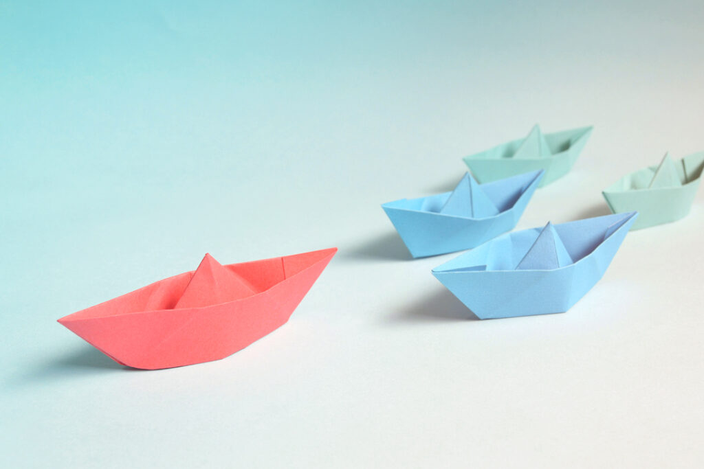paper sail boats following each other representing sustainable leadership