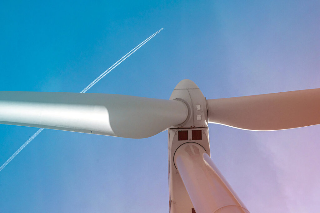 image looking up at a windmill and a plane in the sky above