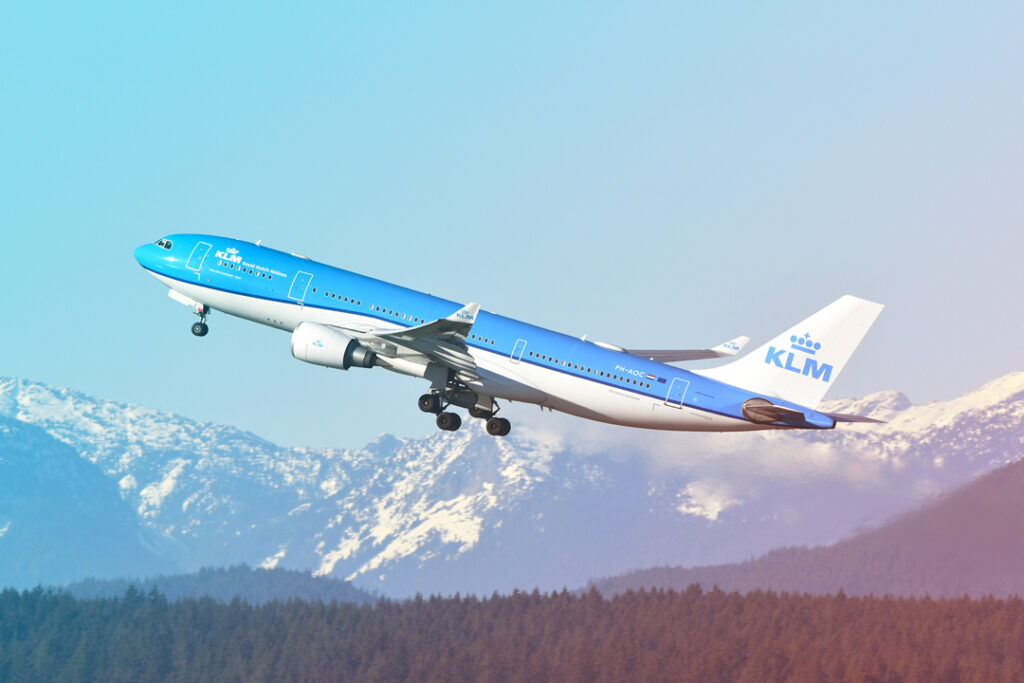 Image of a KLM aircraft taking off with snow covered mountians in the background.