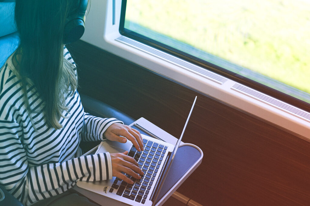 Image of a Traveler taking the train instead of airtravel and working on thier laptom while traveling.