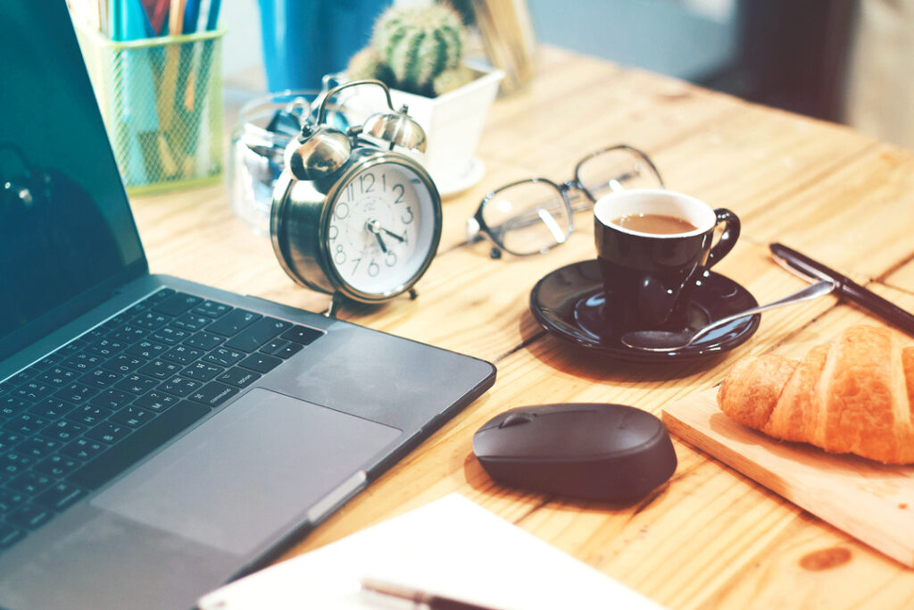 Image of a desk with a laptop, notepad, and cup of coffee on it.