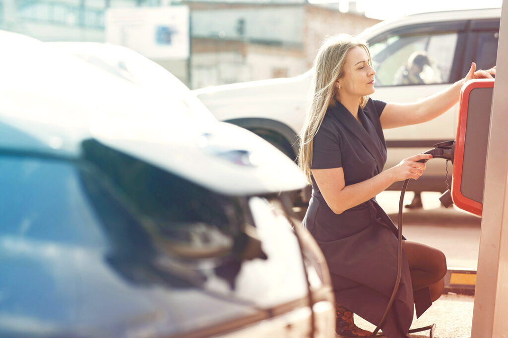 Image of a Traveler charging an electric car. Sustainable corporate travel policies in 2025.