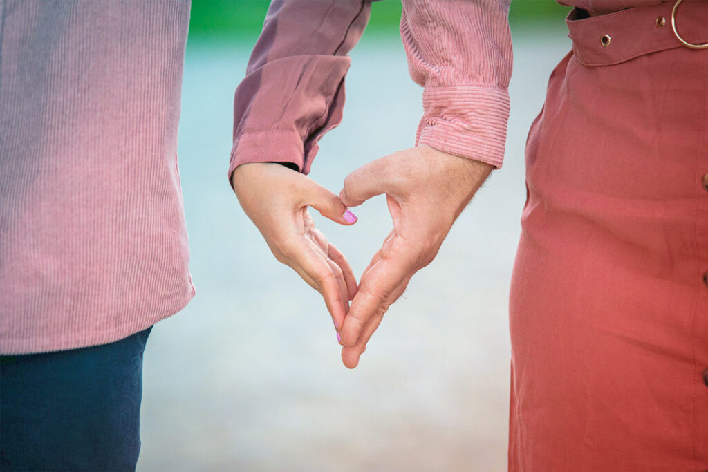 Image of a couple standing, side-by-side, making a heart shape with their hands - business travel during Valentine’s Day