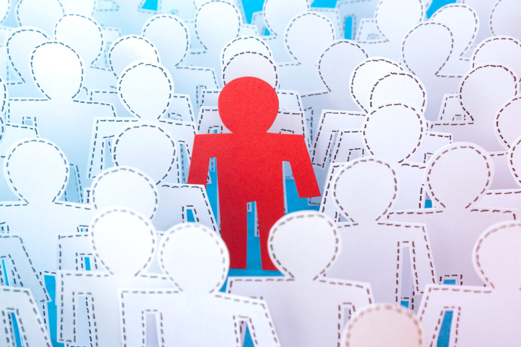 Image of a single red paper cut out of a mad amongst many white cut outs