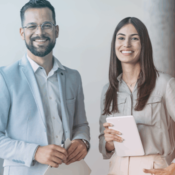 A man and wo,am dressed in business casual, standing next to each other smiling in an office environment.