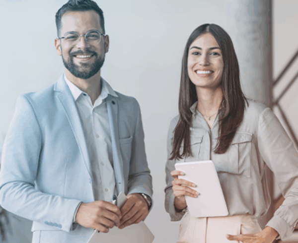A man and wo,am dressed in business casual, standing next to each other smiling in an office environment.