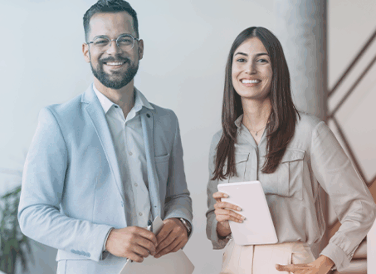A man and wo,am dressed in business casual, standing next to each other smiling in an office environment.