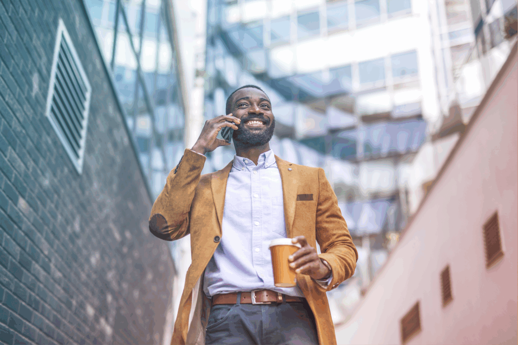 A man in business casual wear is talking on the phone and holding a coffee cup, suggesting a busy professional moment while walking down a staircase in a business park.