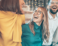 A group of diverse individuals stands together, all laughing joyfully. They are dressed in casual clothing and exhibit expressions of happiness and friendship.