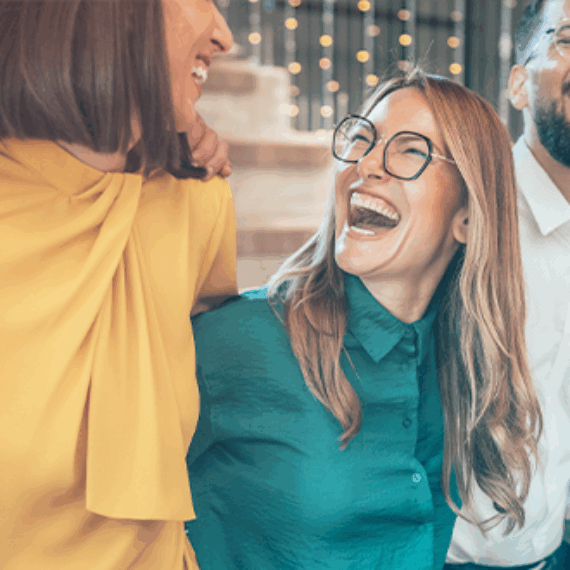 A group of diverse individuals stands together, all laughing joyfully. They are dressed in casual clothing and exhibit expressions of happiness and friendship.