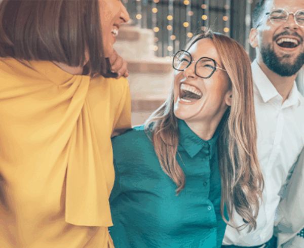 A group of diverse individuals stands together, all laughing joyfully. They are dressed in casual clothing and exhibit expressions of happiness and friendship.