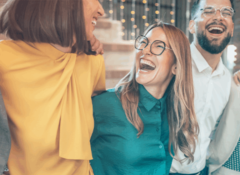 A group of diverse individuals stands together, all laughing joyfully. They are dressed in casual clothing and exhibit expressions of happiness and friendship.
