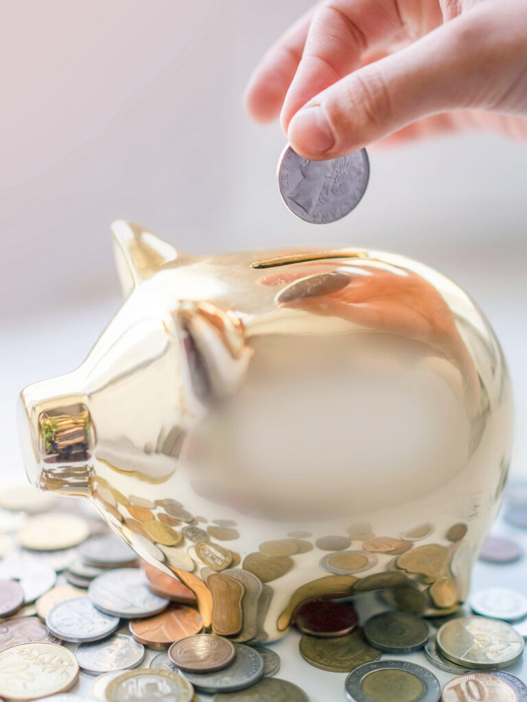 A person adding a coin to a golden piggy bank 