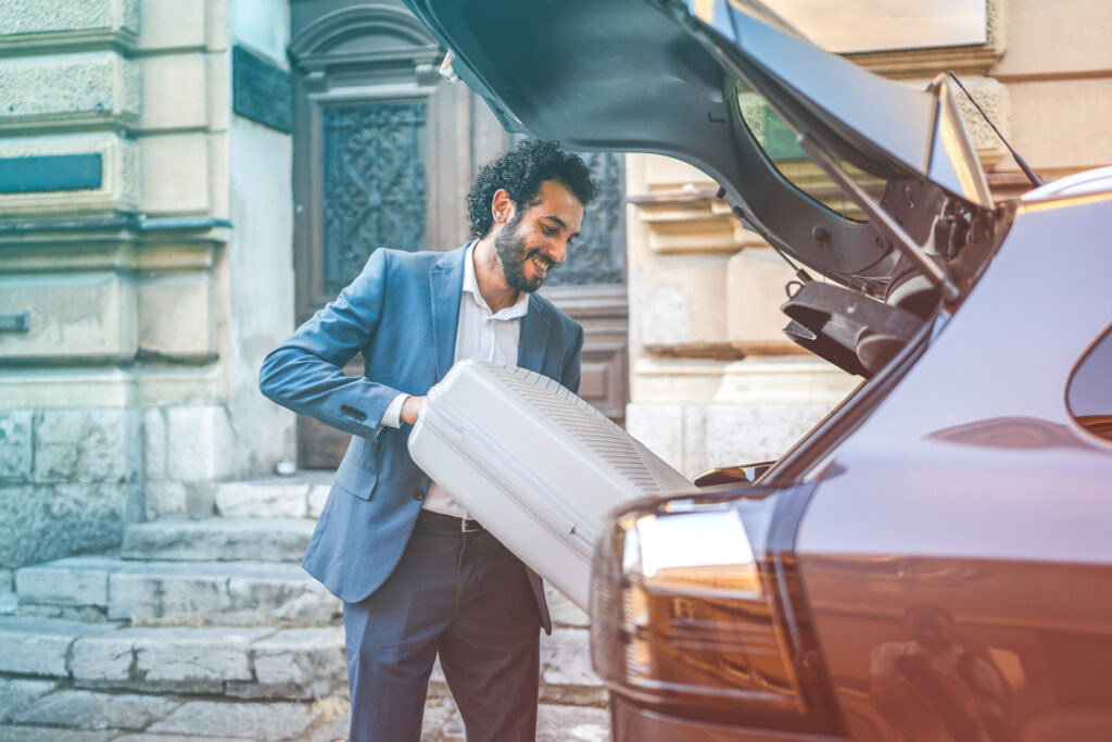 Traveler putting their bags into the trunk of a car.