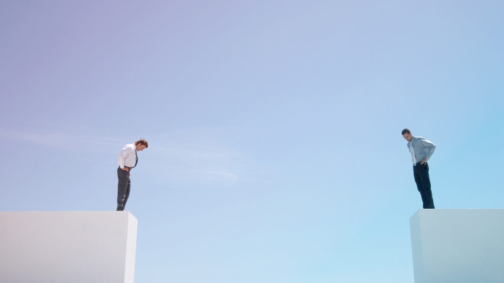 Two Businessmen standing on the edge of a wall, looking down demonstrating the gap between self-managed and managed travel programs